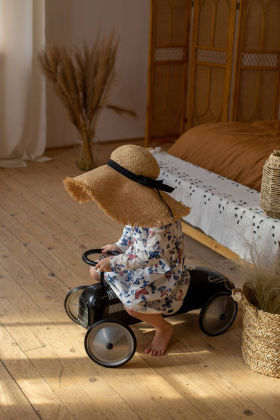 una ragazza in un cappello di paglia divertente cavalca una macchina per bambini intorno alla stanza
 - Foto, immagini