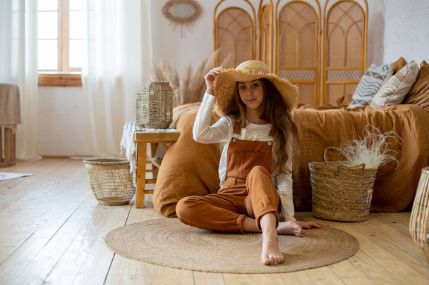 Une jeune fille aux pieds nus portant un grand chapeau de paille s'assoit par terre dans la chambre - Photo, image