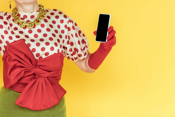 Rajatut näkymä tyylikäs vanhempi nainen tilalla älypuhelin eristetty keltainen
 - Valokuva, kuva