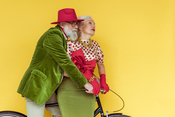 Stylish senior couple looking away on bicycle isolated on yellow - Photo, Image
