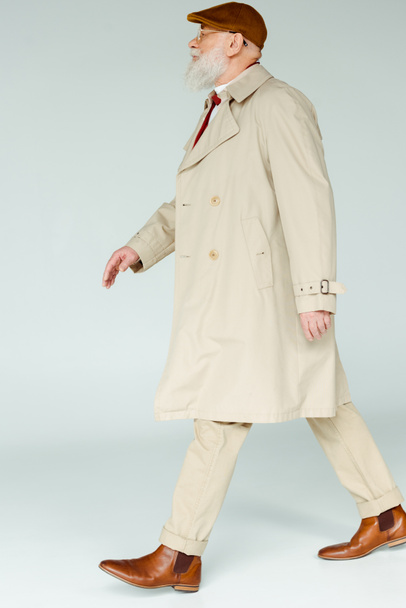 Side view of handsome senior man in coat walking on white background - Foto, afbeelding