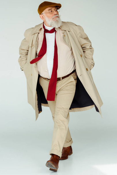 Full length of handsome senior man in trench coat walking on white background - Foto, afbeelding