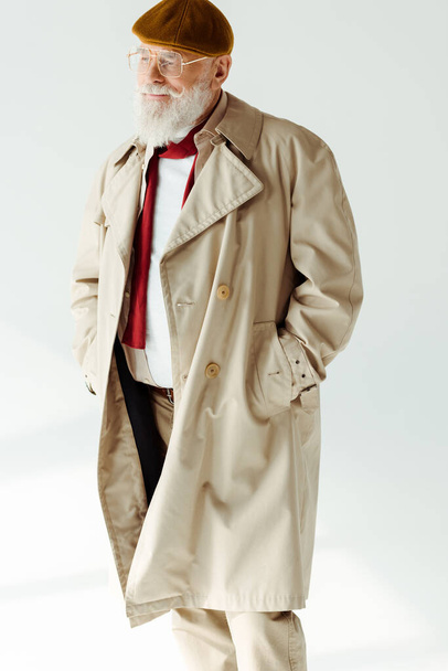 Handsome elderly man in coat and beret looking away on white background - Foto, afbeelding