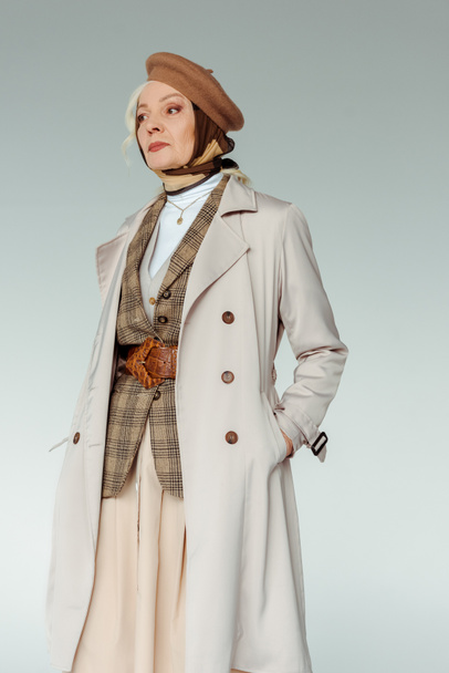 Beautiful senior woman in trench coat and beret looking away isolated on grey - Foto, immagini