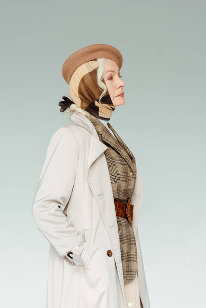 Side view of elegant elderly woman in coat and beret looking away isolated on grey - Foto, Imagen