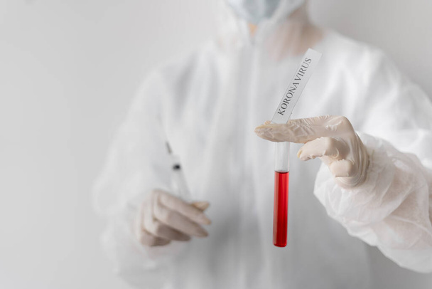 Ein Arzt oder Laborant im Schutzanzug hält ein Reagenzglas mit roter Flüssigkeit in der Hand. Die Inschrift Coronavirus im Labor. Vorsicht mögliche Infektion. Coronavirus 2019-nCoV-Impfstoff - Foto, Bild