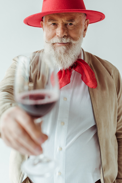 Selective focus of handsome senior man in rd hat holding glass of wine isolated on grey - Фото, изображение