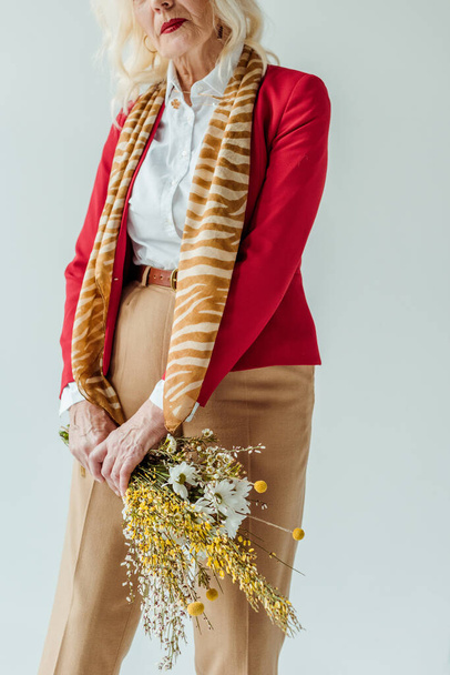 Cropped view of stylish senior woman holding bouquet of wildflowers isolated on grey - Foto, Bild