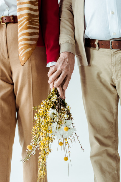 Vista recortada de elegante pareja de ancianos sosteniendo ramo de flores silvestres aisladas en blanco
 - Foto, Imagen