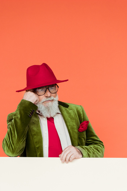 Handsome senior man in jacket and hat looking away on white background isolated on coral  - Fotografie, Obrázek