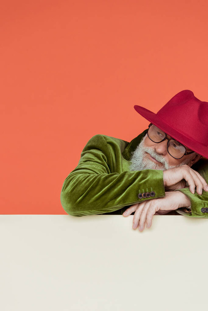 Fashionable elderly man in red hat looking away on white background isolated on coral  - Photo, Image