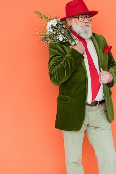 Stylish senior man posing with bouquet of wildflowers isolated on coral  - Foto, afbeelding