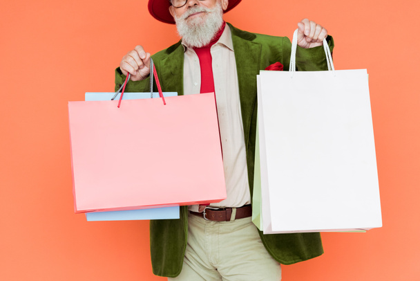 Oříznutý pohled na módní senior muž držící nákupní tašky izolované na korálech  - Fotografie, Obrázek