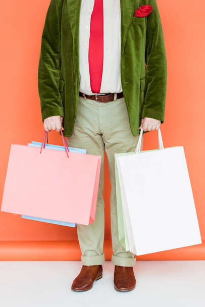 Cropped view of senior man holding shopping bags on white surface on coral background - Фото, изображение
