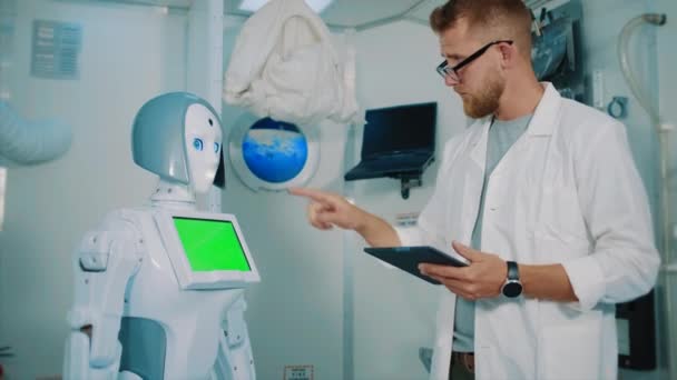 man engineer is programming robot by tablet in laboratory - Materiał filmowy, wideo