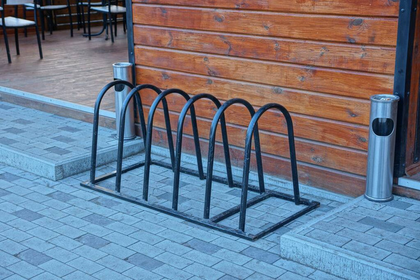 ferro nero parcheggio biciclette si trova su un marciapiede grigio vicino a una parete di legno marrone con urne di metallo
 - Foto, immagini