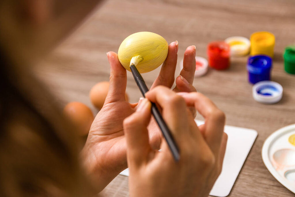 easter mood. close up young woman hands painting easter eggs with brush and gouache in pastel colors over wooden table at home. - Foto, Imagem