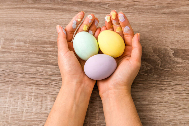 easter concept. closeup beautiful woman hands holding three eggs colored in tender pastel colors yellow, mint and purple over wooden table. - Fotó, kép