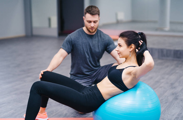 Trainer helping client workout on exercise ball at the gym. Sport and assistance concept. Doing exercises on fitball - Foto, Imagem