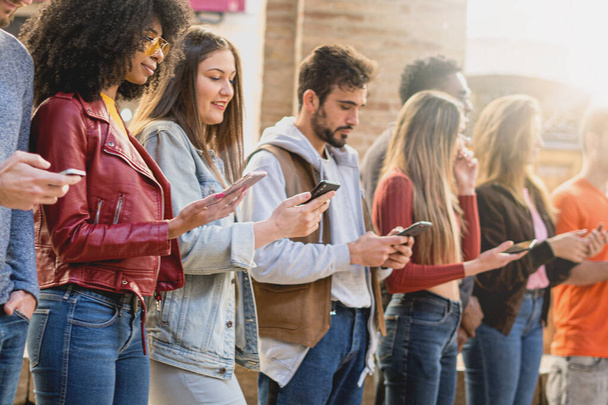 Group of multiracial friends disposed in a raw addicted from social media network. Students using smartphone and internet addiction concept.  - Photo, Image