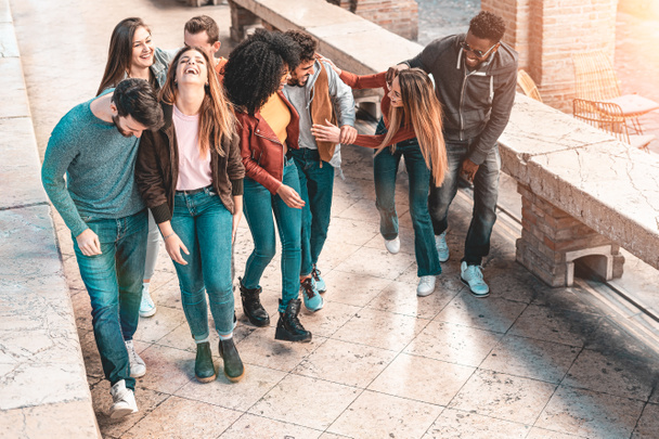Mixed race group of young people smiling and having walking together and chatting outdoors in the street. Boys and girls lifestyle concept. Teal and orange filtered image - Photo, Image