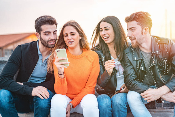Bir grup genç milenyum insanı akıllı telefon kullanarak eğleniyor. Genç arkadaşlar sosyal medya uygulamasında komik bir video izliyor ve birlikte gülüyorlar. - Fotoğraf, Görsel