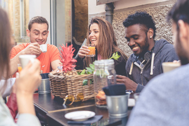 Wielorasowi przyjaciele, dziewczyny i faceci, śmiejący się z picia kawy w kawiarni, szczęśliwi młodzi ludzie gadający żarty siedzący razem przy stoliku kawiarni, wielokulturowa koncepcja przyjaźni - Zdjęcie, obraz