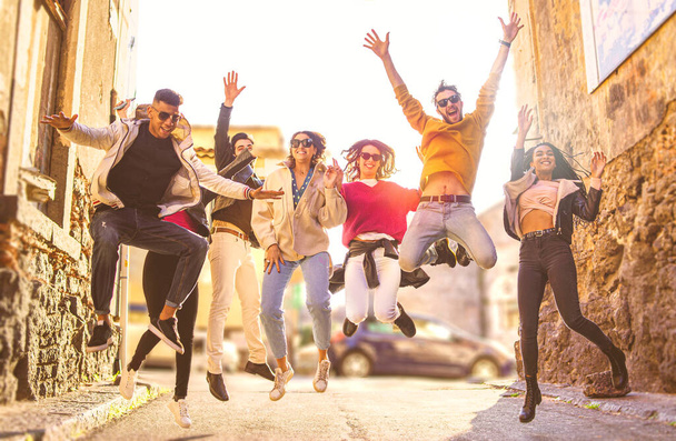 A fiatalok többnemzetiségű csoportja városi környezetben szórakozik együtt a szabadban. Egy csapat barát együtt ugrál az utcán egy napsütéses napon. Az összetartozás fogalma. - Fotó, kép