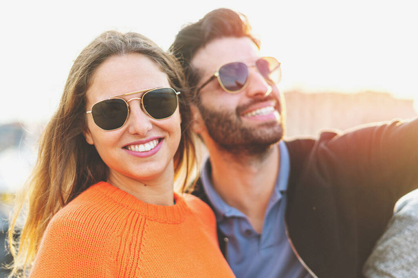 Beautiful couple of young people wearing sunglasses enjoying life in the summer. She's looking at the camera. - Photo, Image