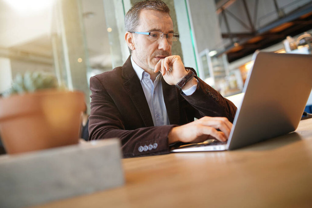 Businessman working in coffee shop on laptop computer - 写真・画像