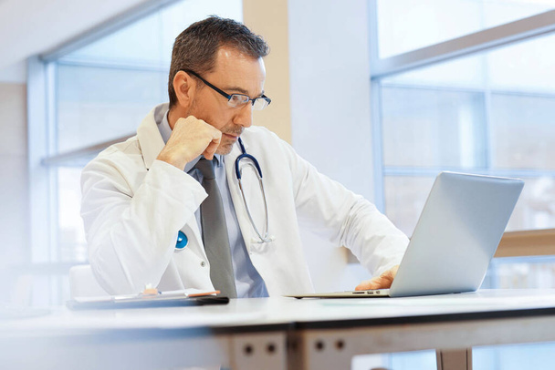 Doctor in hospital office working on laptop - Foto, afbeelding