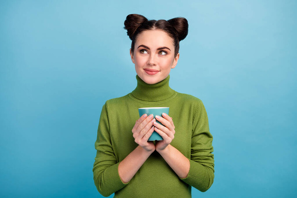 Photo of attractive teen lady hold hot beverage cup tea enjoy weekend morning look empty space dreamer wear warm green turtleneck sweater isolated blue color background - 写真・画像