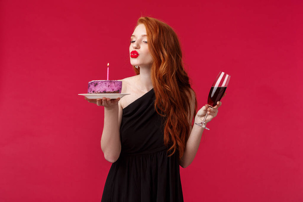 Ritratto di elegante bella donna rossa femminile con rossetto rosso, trucco serale e vestito nero, festeggiando il compleanno alla festa con vino rosso e b-day cake, soffiando sensualmente candela
 - Foto, immagini