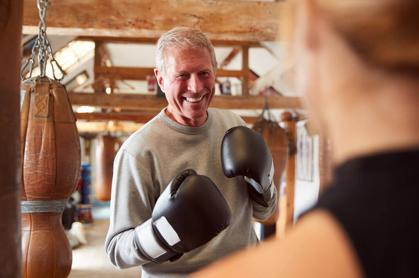 Senior Male Boxer Sparring With Younger Female Coach In Gym Using Training Gloves - Photo, image