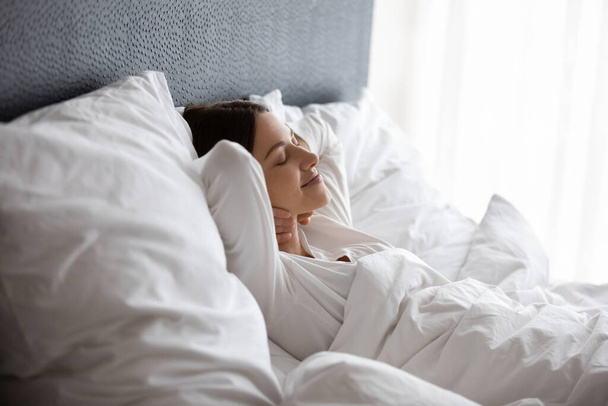 Γαλήνια ήρεμη ευτυχισμένη νεαρή γυναίκα κοιμάται στο κρεβάτι. - Φωτογραφία, εικόνα