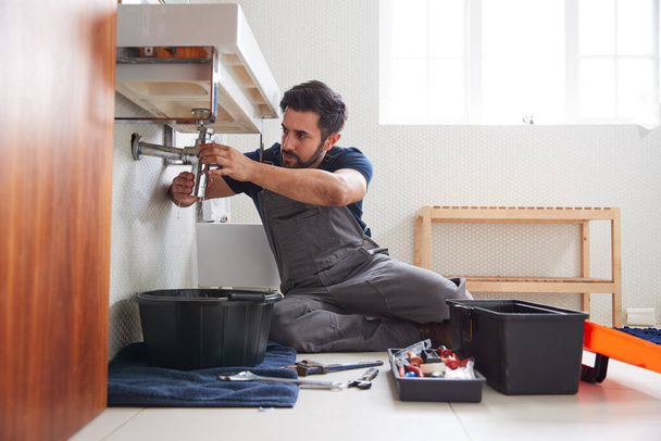 Male Plumber Working To Fix Leaking Sink In Home Bathroom - Foto, Imagen