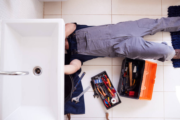 Overhead Shot Of Male Plumber Working To Fix Leaking Sink In Home Bathroom - Φωτογραφία, εικόνα