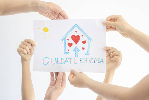 スペインにおけるコロナウイルスのパンデミック自己隔離。スペイン語の単語を使って子供の絵を描く家族の手クイートen casa -家にいる - 写真・画像
