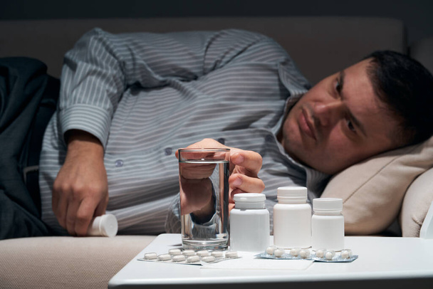 Overworked businessman is lying on the sofa and resting. Pills and glass of water near him. - Photo, Image