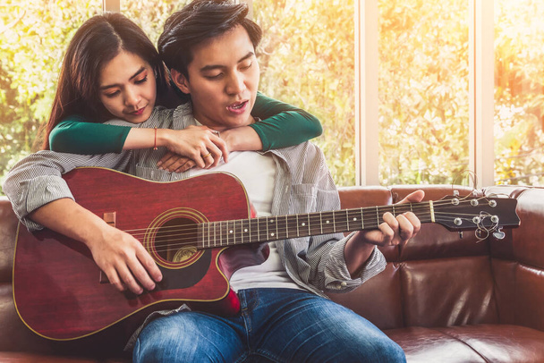 Joven pareja asiática toca guitarra y canta canción en la sala de estar en casa juntos. Concepto de música y estilo de vida
. - Foto, Imagen