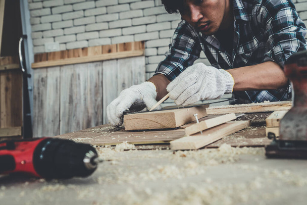 建設材料や木製の家具を生産するためにワークショップで木工に取り組んで大工。若いアジアの大工は作るための専門的な用具を使用する。DIYメーカーと大工仕事のコンセプト. - 写真・画像