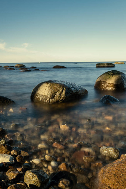 słoneczna plaża z błękitną wodą i dużymi skałami w piasku. Łotwa pod czystym niebem - Zdjęcie, obraz