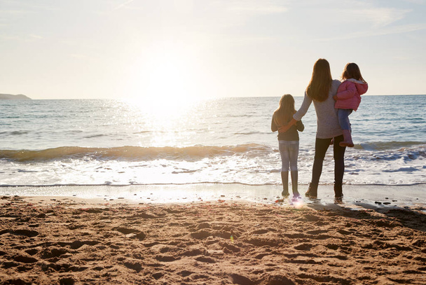 Rear View Of Mother With Daughters Looking Out To Sea Silhouetted Against Sun - Фото, изображение