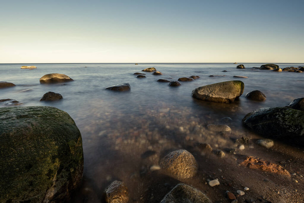 praia ensolarada com água azul e grandes rochas na areia. Letónia sob céu limpo
 - Foto, Imagem