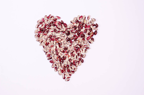Feijão roxo seco para veganos na forma de um coração em um espaço de cópia de fundo branco. Alimentos saudáveis ricos em proteínas e carboidratos. Vista de cima
. - Foto, Imagem