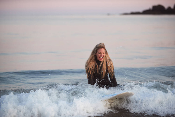 Woman Wearing Wetsuit Sitting On Surfboard Riding Wave Into Beach - Fotoğraf, Görsel