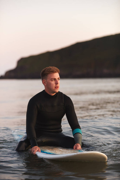 Man Wearing Wetsuit Sitting And Floating On Surfboard On Calm  Sea - Фото, изображение