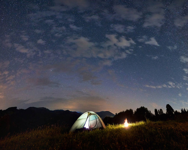 Φωτιζόμενη σκηνή και φωτιά κάτω από απίστευτο έναστρο ουρανό, καλοκαιρινό βράδυ στα βουνά, ομορφιά της φύσης. Νυχτερινό κάμπινγκ - Φωτογραφία, εικόνα