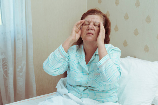 Ηλικιωμένη γυναίκα αισθάνεται άρρωστος στο σπίτι στην κρεβατοκάμαρα. - Φωτογραφία, εικόνα
