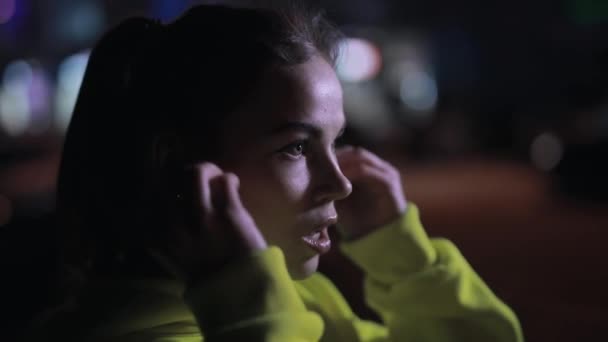 Pewna siebie sportowiec zakłada słuchawki bezprzewodowe w nocy - Materiał filmowy, wideo